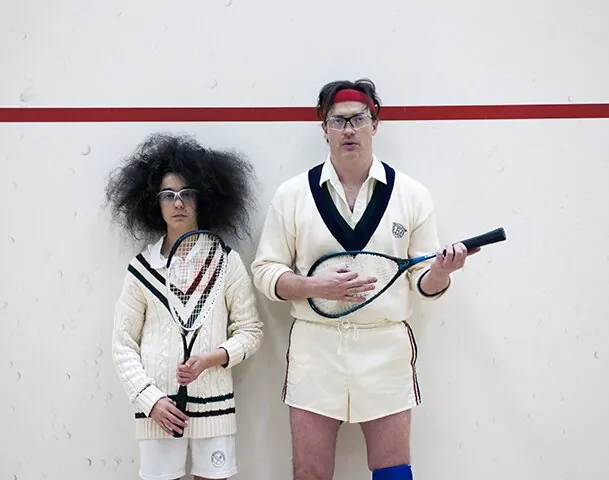 Two students in athletic uniforms at a squash court